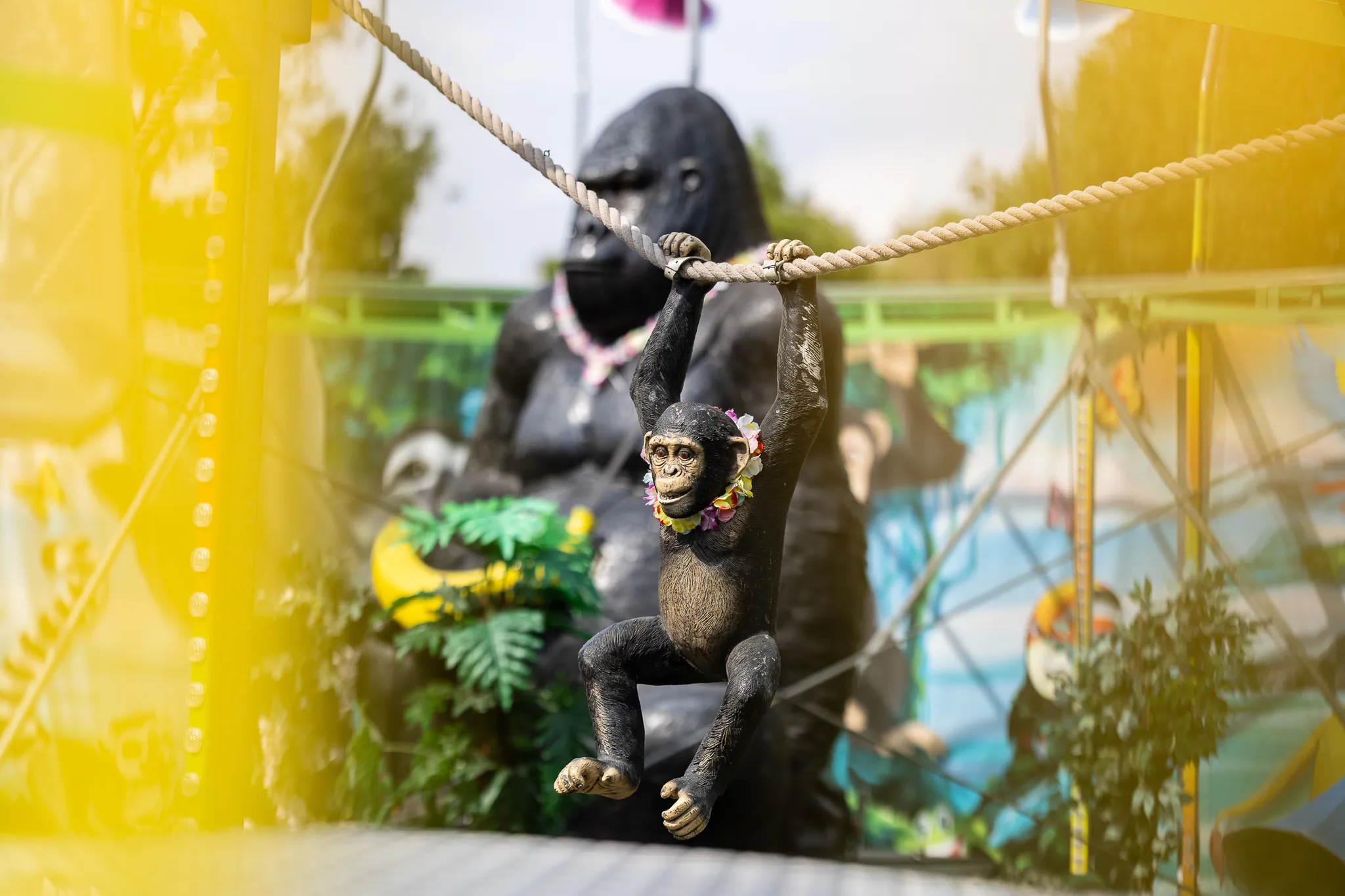 Eine kleine Affenfigur hängt an einem Seil; dahinter ist eine große Gorillastatue unscharf zu sehen.