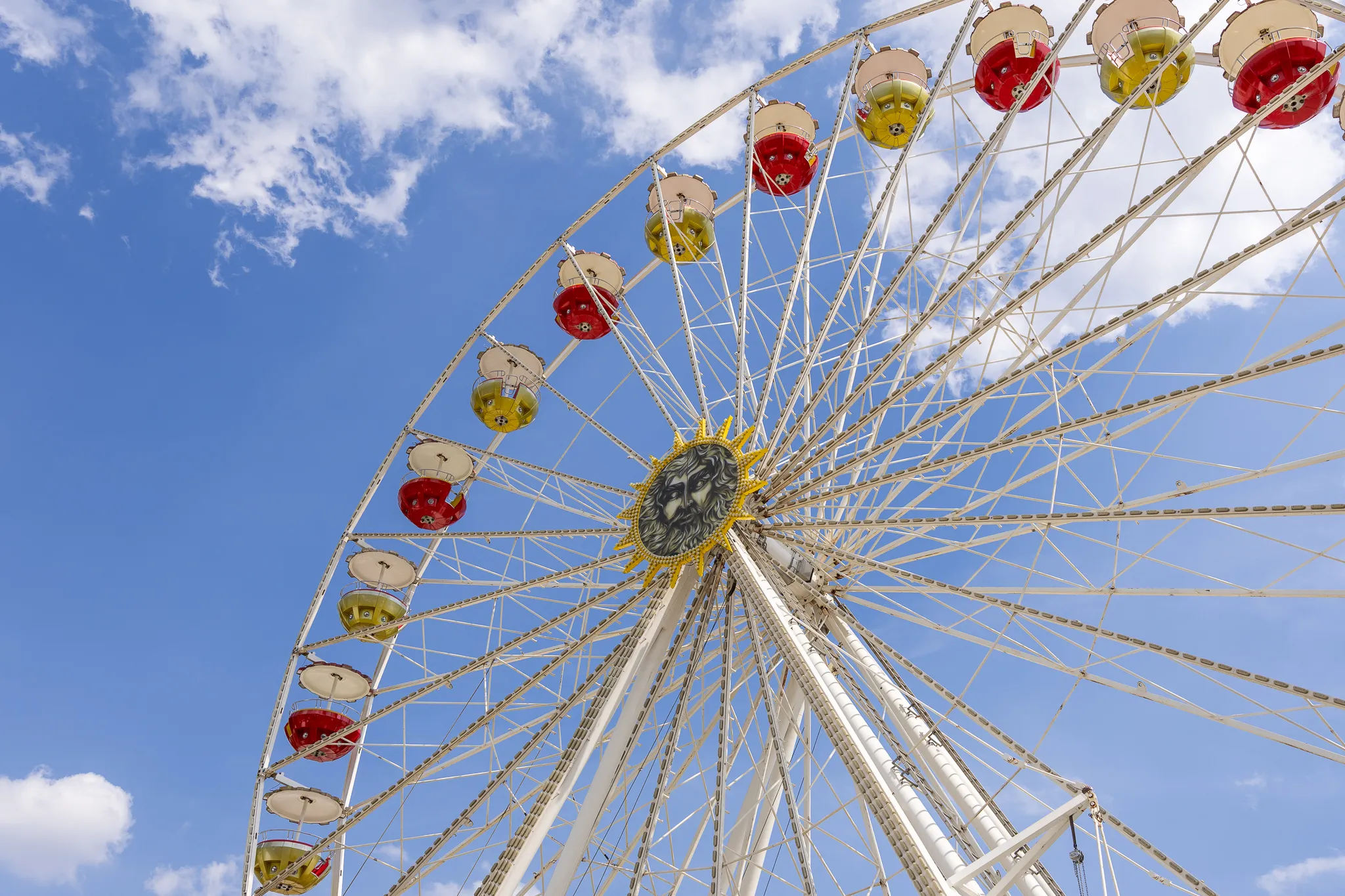 Das weiße Riesenrad steht mit roten und gelben Gondeln vor blauem Himmel.