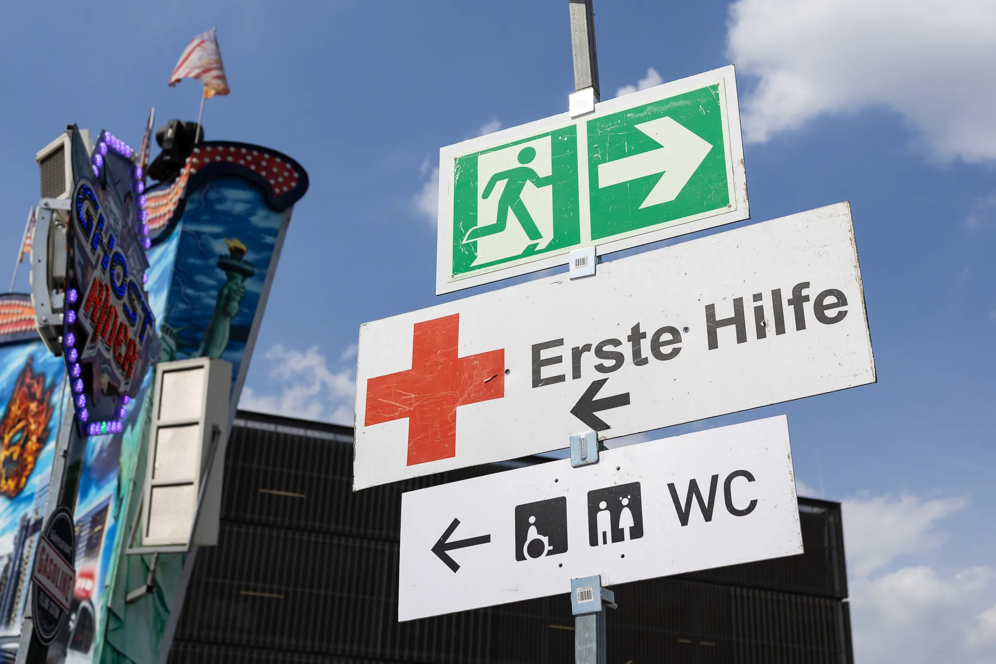 Wegweiser zeigen zu einem Notausgang, zur Ersten Hilfe und zu Toiletten.