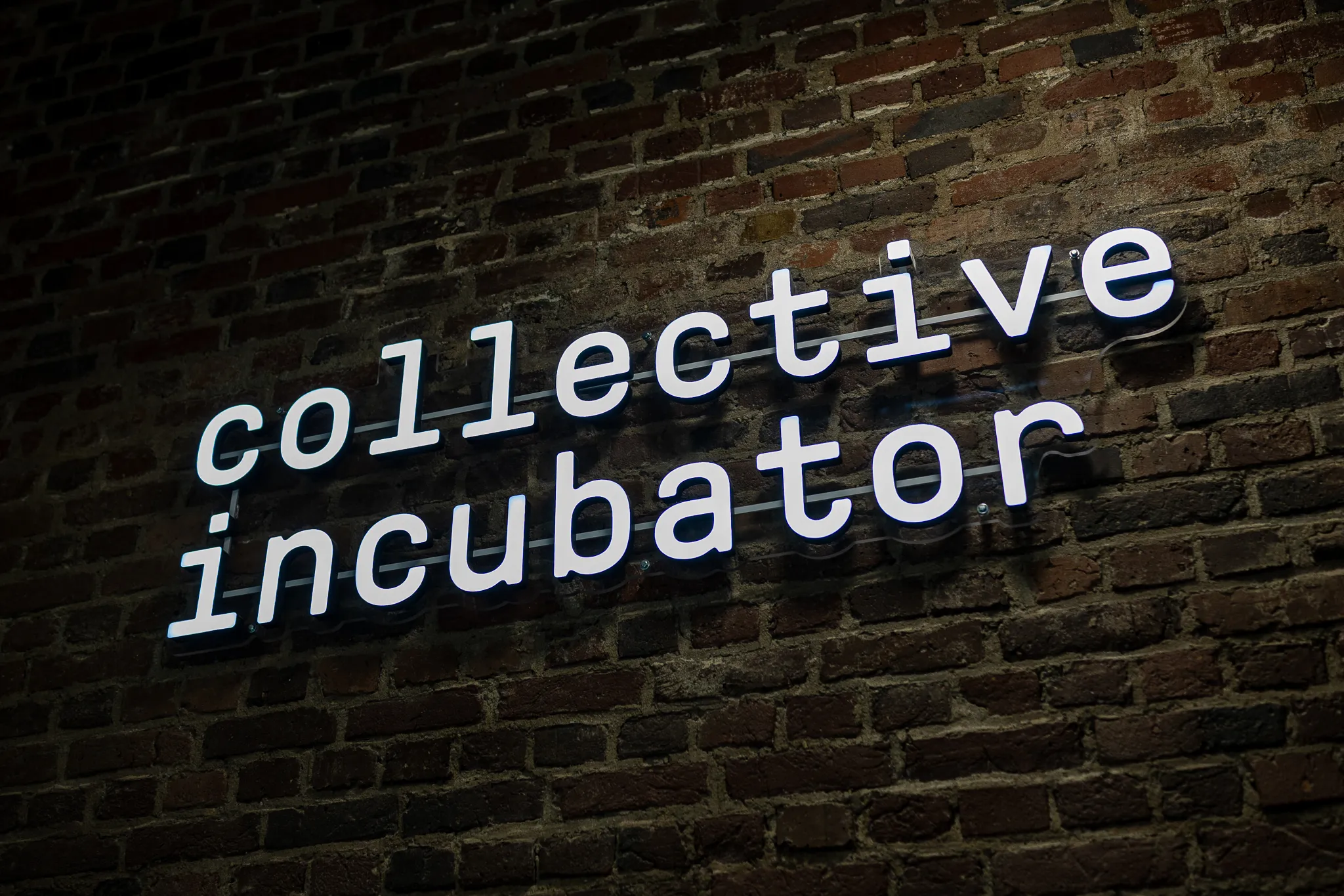 Leuchtschrift des Collective Incubators vor einer Backsteinwand.