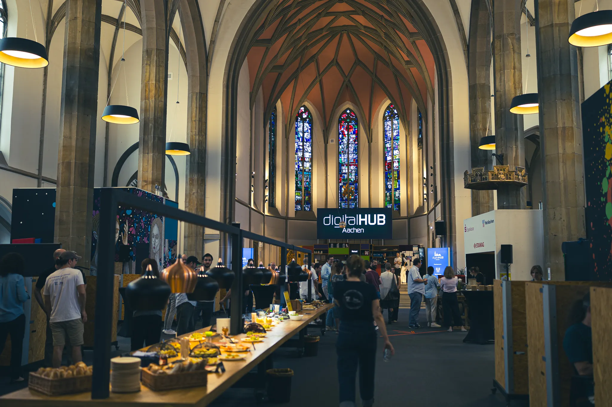 Frühstücksbuffet im Kirchenschiff der digitalCHURCH mit Gästen und Fensterkunstwerken im Hintergrund.